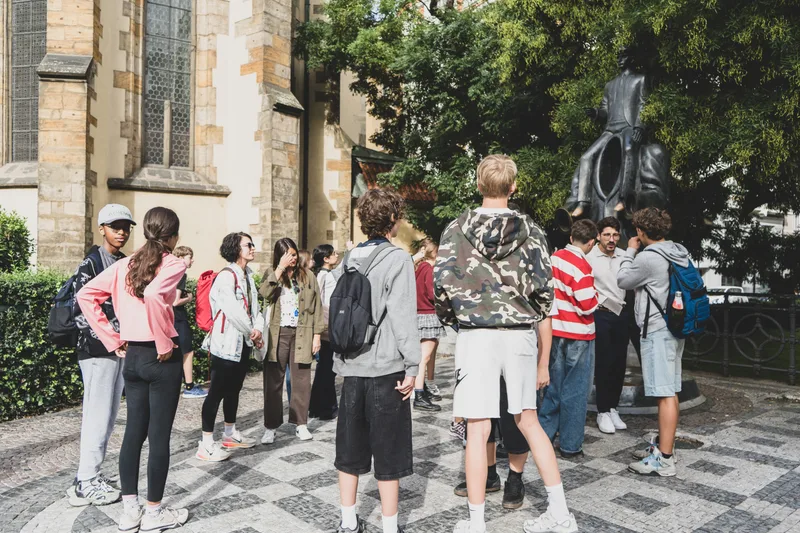 Malá skupina studentů s dospělým doprovodem u sochy v centru Prahy během Treasure Huntu